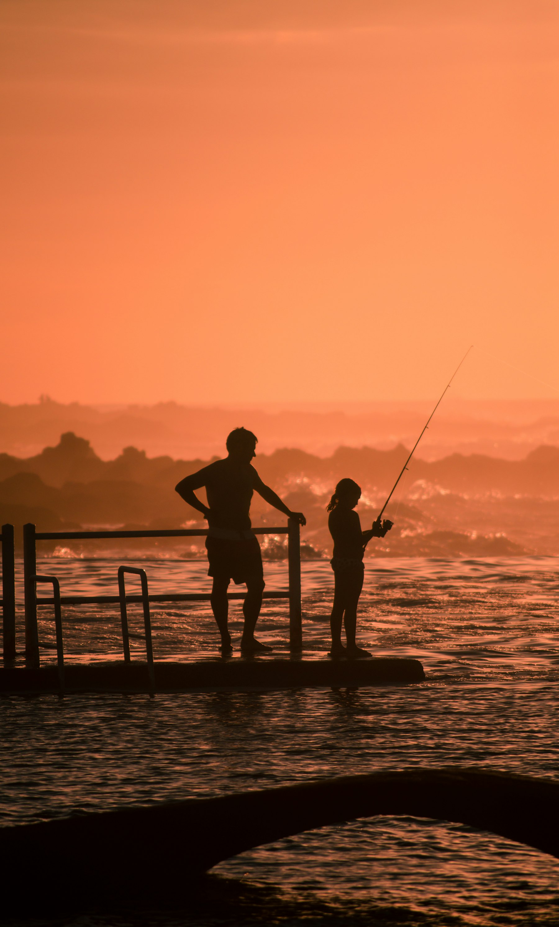 A father and daughter fishing together in silhouette at sunset