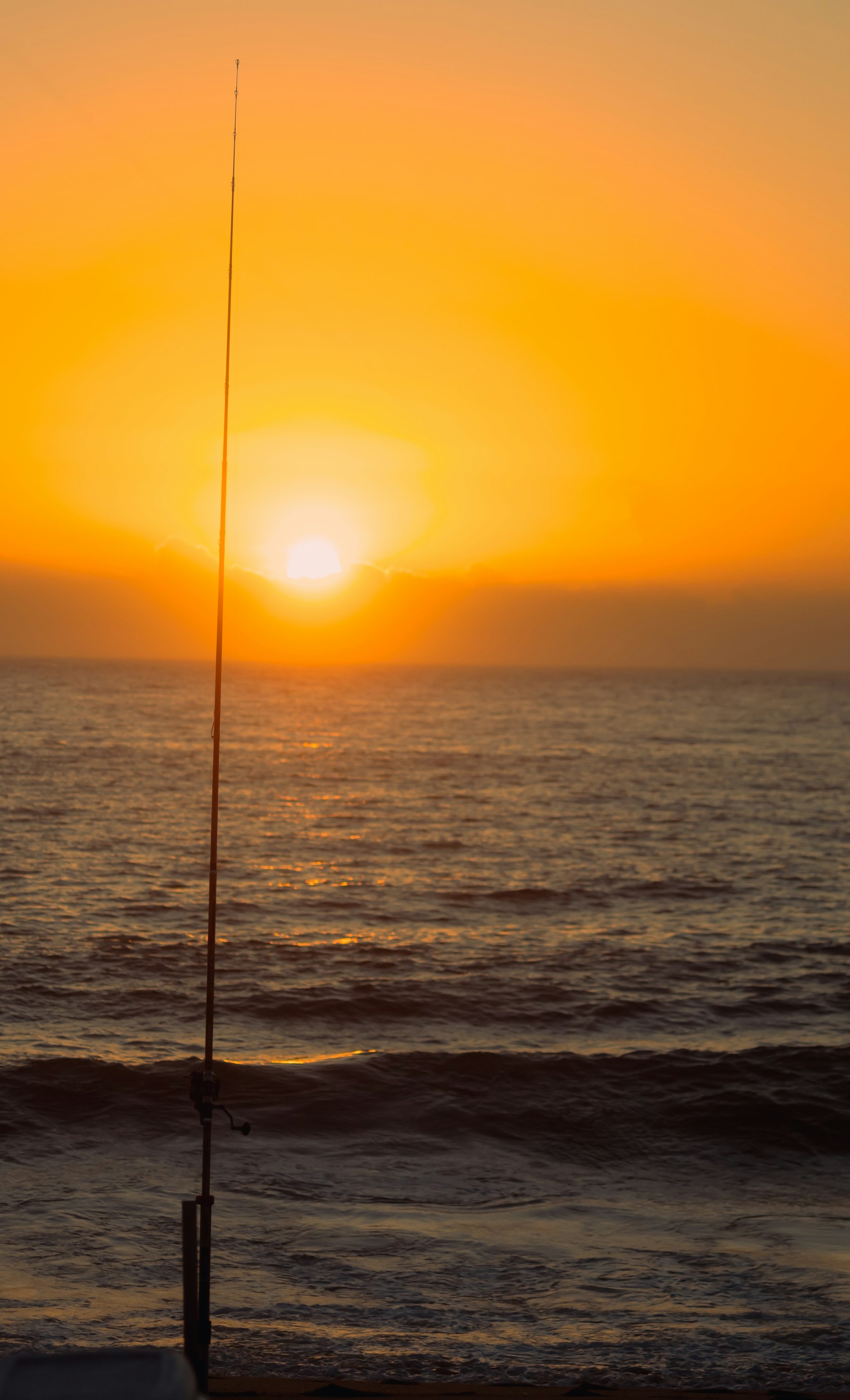 A fishing rod planted in the sand at sunset